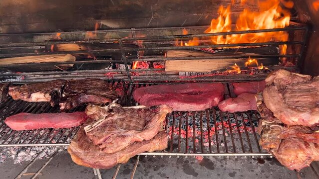 Barbeque with steaks and beef chops on grate over coals and fire in the background