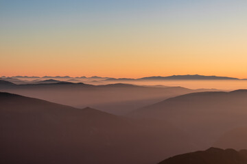 Panoramic sunrise view from Dobratsch on High Tauern and Nocky Alps in Austria, Europe. Silhouette of endless mountain ranges covered by mystical fog in valley. Jagged sharp peaks and alpine landscape