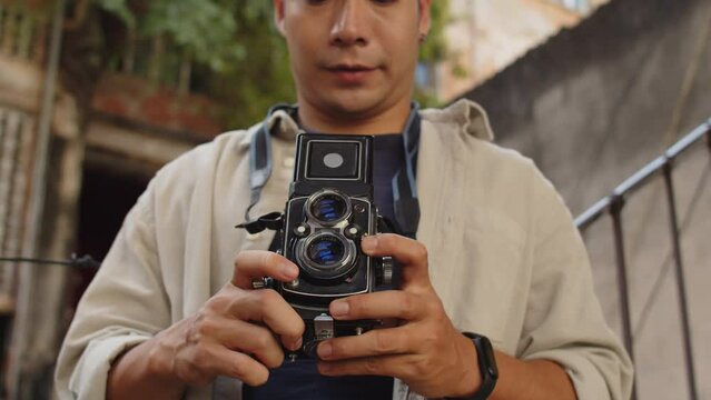 Tilt down shot of positive Asian man using old camera capturing exteriors of old buildings in photograph