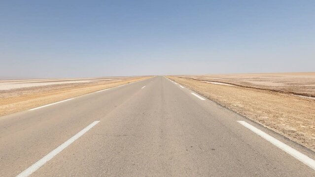 Driving on empty highway crossing the Chott el Djerid salt pan, Saharan desert landscape in Tunisia