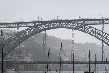 Masts of wooden rabelos boats docked on the Douro River in Porto, under the Don Luis I steel bridge...
