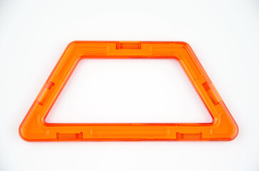 Orange plastic trapezoid from transparent magnet constructor kit (puzzle builder for kids) isolated on a white background