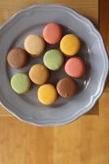 Purple plate filled with pastel macarons on wooden table. Top view.