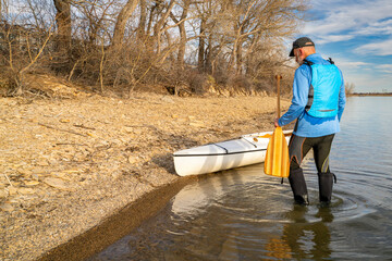 senior male paddler with expedition decked canoe on a lake shore in early spring, Boedecker Reservoir in northern Colorado - 779985569