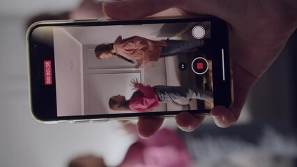 A hand of woman photographer holds a smartphone and takes a video of two girls. Cheerful and energetic teenagers dance and play with palms in front of the camera. Close up. Blur effect.