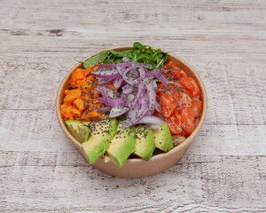 Takeaway poke bowl with fresh salmon, avocado and vegetables in recycled kraft paper packaging....