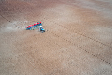Obraz premium Spring. Sowing. Panoramic aerial view of a tractor with a trailed seeder working on a field. Copy space.