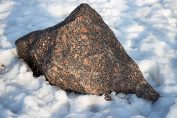 A large stone lies in the snow, winter and sunny day.