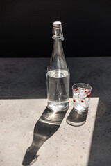 objects and drinks concept - bottle of water and glass with ice and cranberries on sunny floor