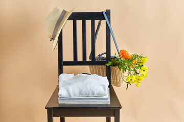 home decor and design concept - flowers in wicker bag or basket, clothes, hat and magazines on vintage chair over beige background