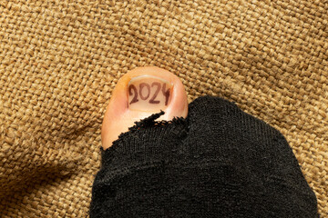 2024 is drawn on a girls toe that sticks out of a torn sock, poverty