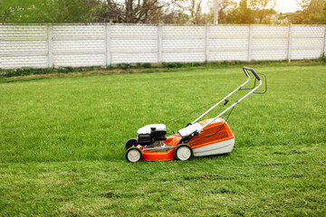 Top view of modern orange-grey gasoline lawn mower cutting bright lush green grass. Gardening work tools. Rotary lawn mower machine on lawn. Professional lawn care service. Place for text