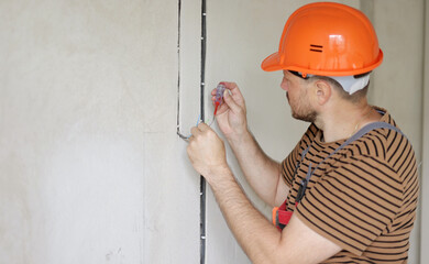 male electrician hands checks presence of electrical voltage in socket phase uses electrical tester screwdriver. Examining three coloured wires in outlet by voltage detector indoor - obrazy, fototapety, plakaty