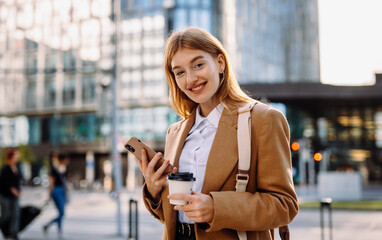 A woman in a blazer smiles at her phone in the city