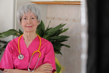 Senior female nurse wearing pink scrubs and yellow stethoscope 