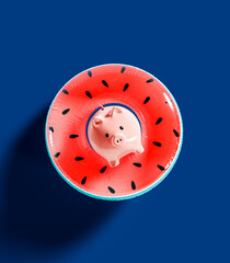 Piggy bank with Watermelon inflatable rubber ring on vibrant blue background. Savings for summer vacation. 3D Rendering, 3D Illustration - 780041918