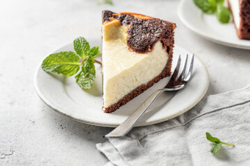 Piece of homemade chocolate cheesecake with mint leave on a plate on white textured background