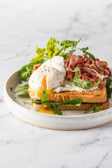 Toasts sandwich with poached egg, arugula, bacon and cream cheese on white plate marble background. Isolated, text space