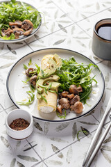 French rolled omelette stuffed with cream cheese with avocado, aragula and mushrooms for breakfast on white plate printed tile background, text space