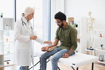 Efficient general practitioner checking solution for chemotherapy of male sitting on exam couch. Young bearded man in casual wear taking dropper while mature female making system review.