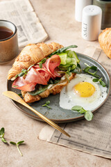 Fresh croissant sandwich with prosciutto or ham, cucumber, soft cheese and micro green and fried egg for breakfast