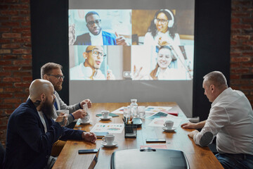 Businessmen sitting in office and having online conference with employees via TV screen. Connecting...