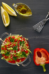 Vegetable salad of raw cabbage and bell pepper, dressed with olive oil and lemon, surrounded by ingredients on a black concrete table