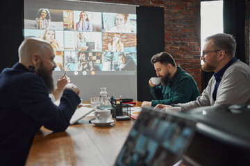 Business professionals gathering in conference room, using video conferencing technology to connect...