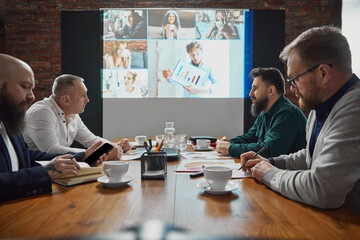 Business leaders sitting conference room, having online video call with employees, promoting...