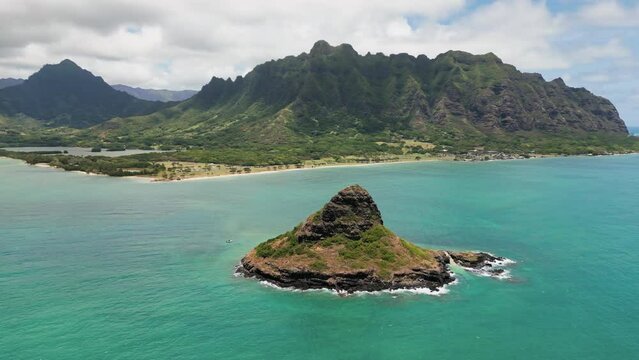 Aerial view of teal blue Pacific ocean with scenic high green mountains covered with rainforest and China Hat on Oahu Island, Honolulu, Hawaii. High quality 4k footage