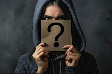 An anonymous woman holds a cardboard sign featuring a question mark, symbolizing curiosity and mystery - obrazy, fototapety, plakaty