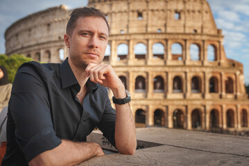 Man in dark shirt looks contemplative near iconic Colosseum in Rome, Italy. Stone ruins in background with warm lighting. Reflection and heritage vibes.