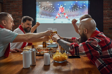Sports enthusiasts, friends gathering at home to watch online hockey game on TV, with beer and...