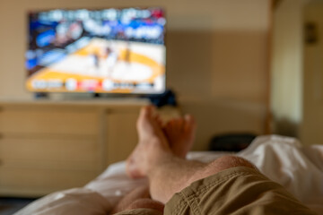Selective focus on propped up feet with a blurred basketball game on the TV - obrazy, fototapety, plakaty