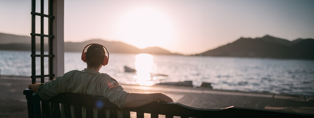 Portrait from the back of a young man in bright big headphones by the sea at sunset. A handsome guy...