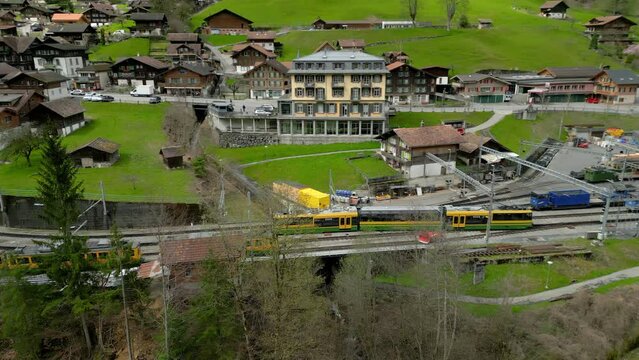 Swiss passenger train with tourists passing by beautifull alpine village in Switzarland, Europe - aerial view from drone. High quality 4k footage