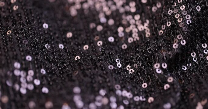 a large number of sequins on a black material, a part of the black material decorated with plastic discs to create shine