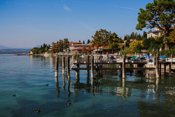 Fototapeta na wymiar City of Sirmione on Lake Garda, wooden pier with built-up lake shore, Italy, Europe.