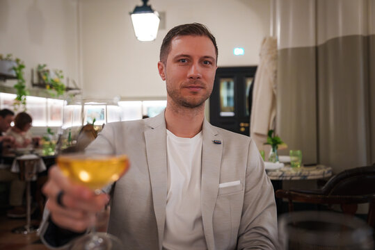 Man in beige suit enjoying drink in luxury hotel dining area in Rome. Sophisticated ambiance, elegant decor, leisurely experience captured in the image.