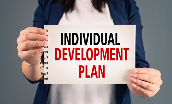 A woman holding a notepad with "individual development plan" written on it, on a gray background, stock photo