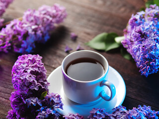 A white cup of tea on a wooden table with blooming lilac branches