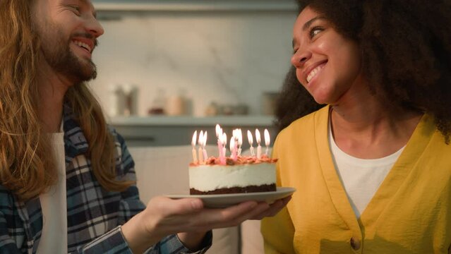 Multiracial couple multiethnic diversity people married Caucasian man boyfriend holding cake for African American birthday woman girlfriend wish blowing candles congratulations celebration at home