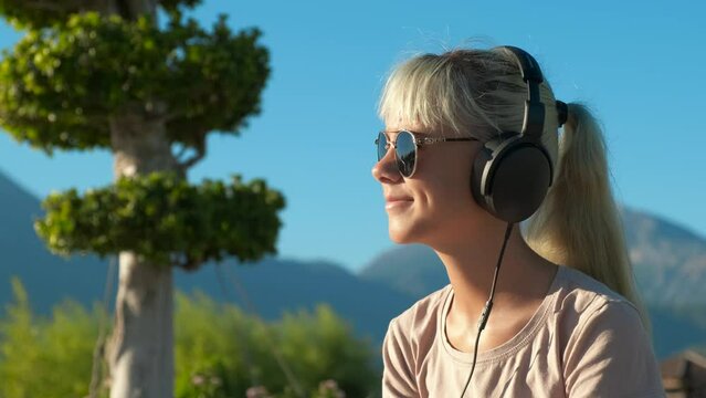 Free beach time with headphones. A view of sunny beach with green nature and relax teen girl in headphones.