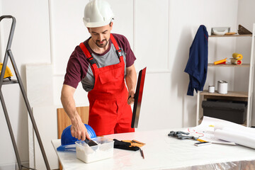 Male decorator with putty knives working in room
