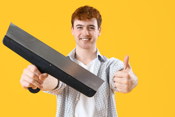 Young man with putty knife showing thumb-up on yellow background