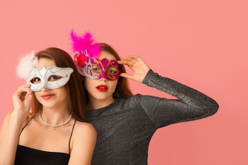 Beautiful young women in carnival masks on pink background