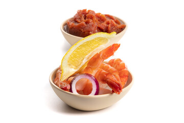 Cooked Black Tiger cocktail shrimp with a slice of lemon in a small bowl with a bowl of seafood cocktail sauce in the background isolated on white
