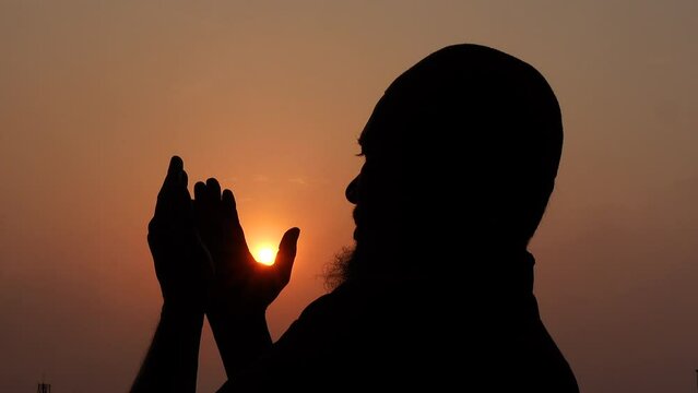 A Muslim old man praying with his hands raised to the sky in the afternoon twilight.