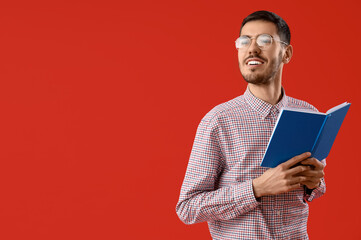 Young man in eyeglasses with book on red background
