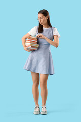 Young woman in eyeglasses with stack of books on blue background